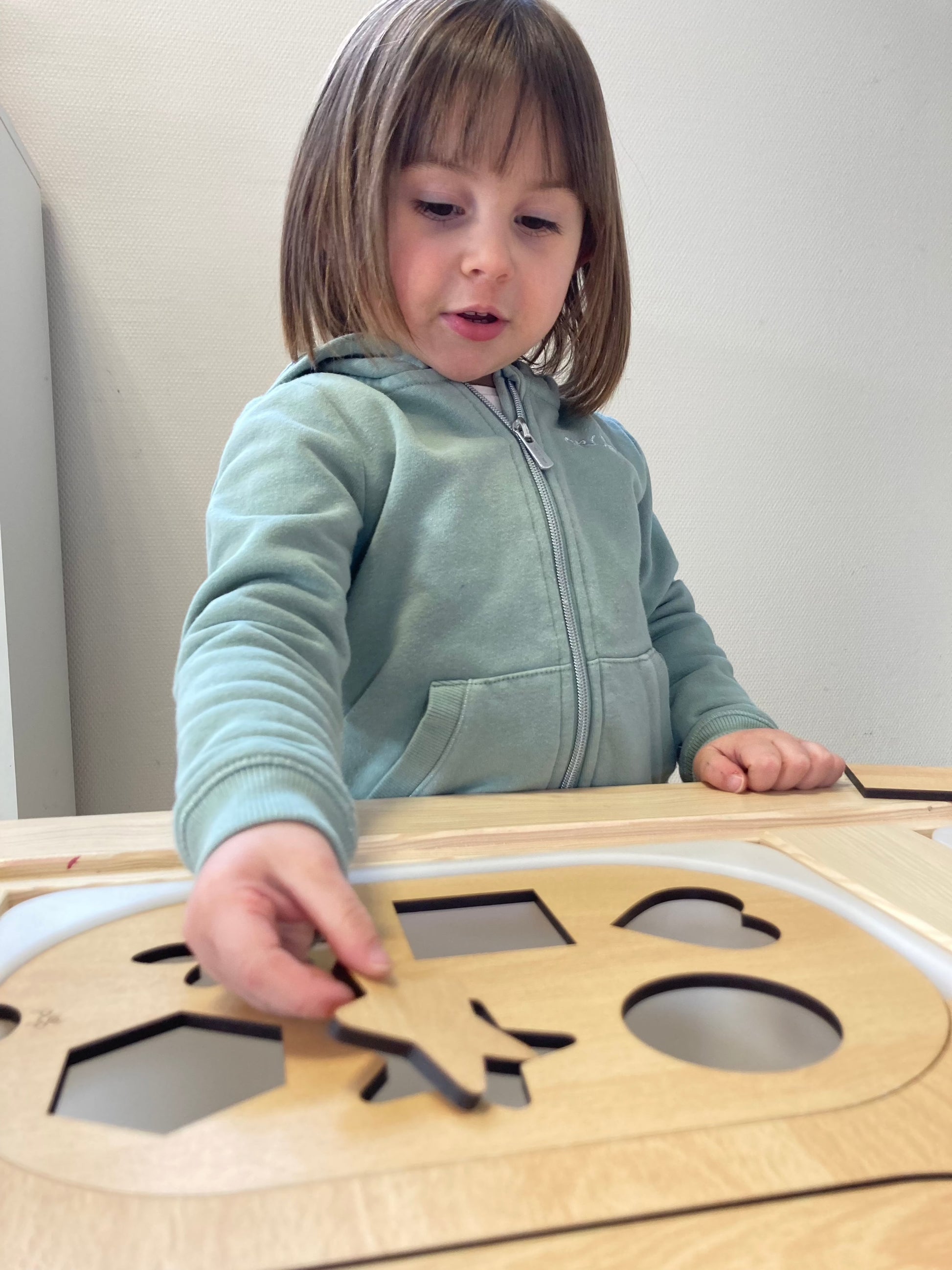 Enfant jouant avec la planche à formes Montessori, encastrant une pièce en bois dans la découpe correspondante pour développer sa motricité fine