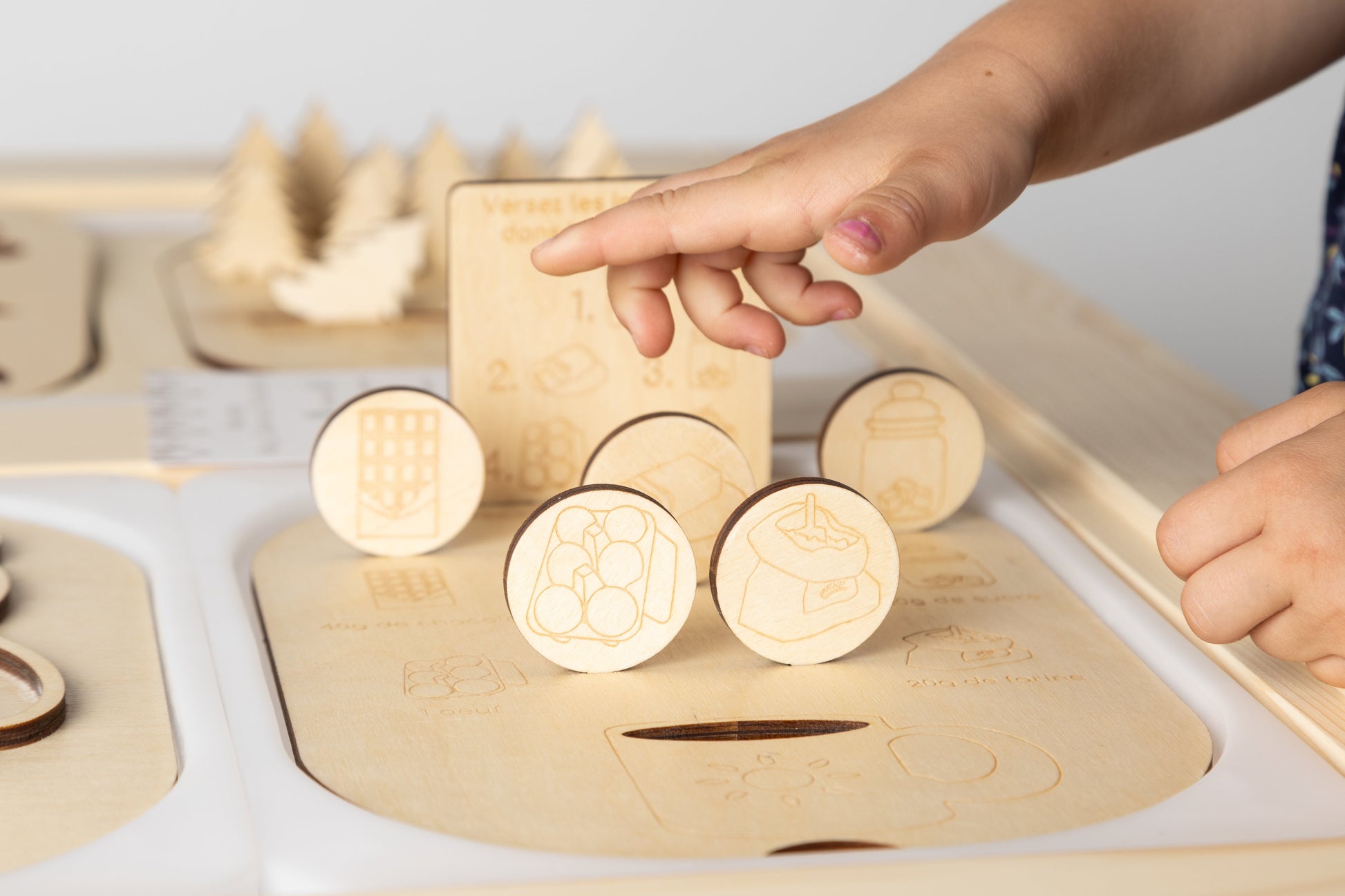 Main d’un enfant manipulant les pièces de la planche Montessori Le Mugcake, représentant les ingrédients pour une activité éducative interactive