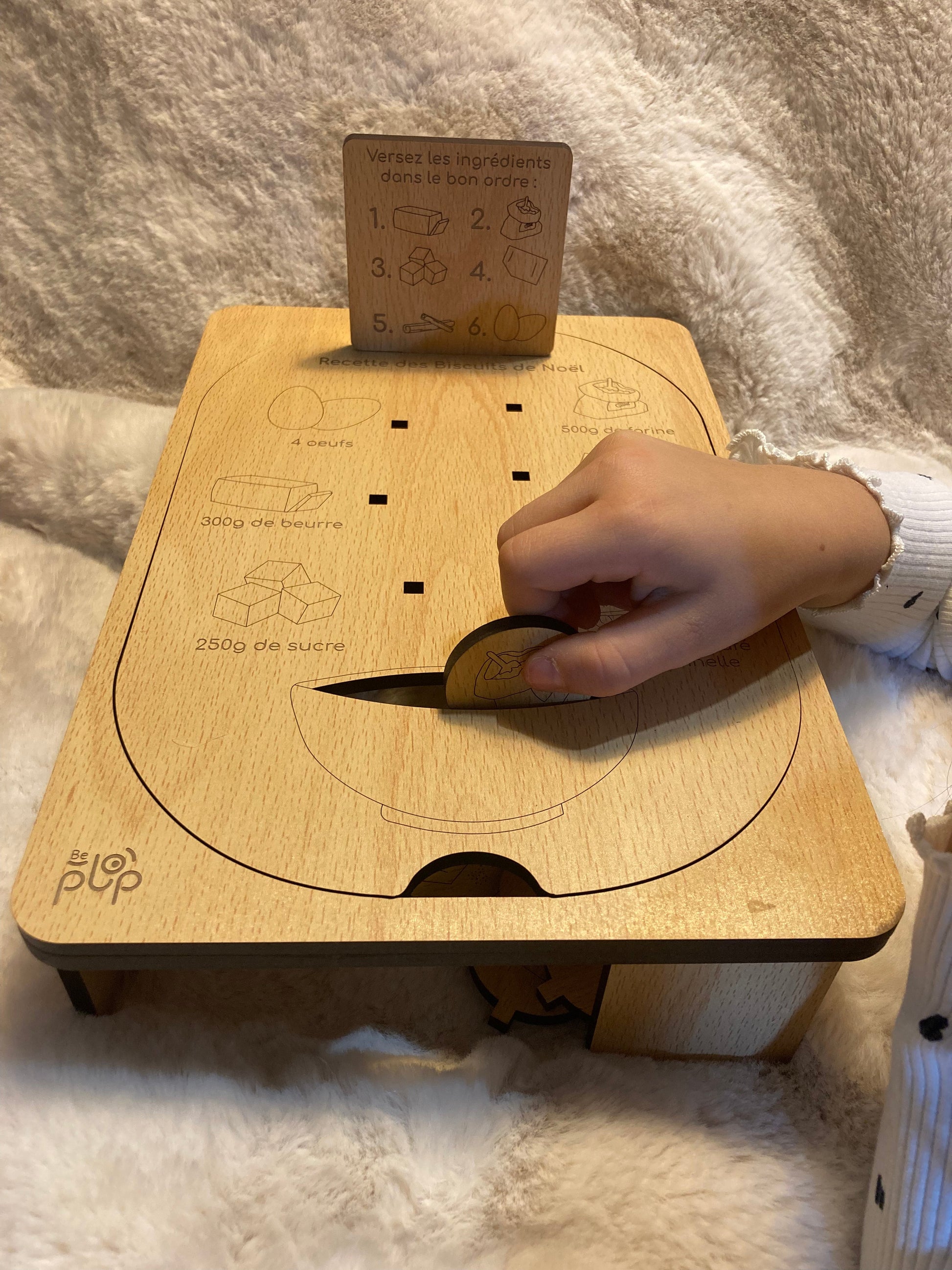 Main d’un enfant insérant une pièce en bois dans une planche Montessori avec des instructions gravées, montée sur un support robuste.